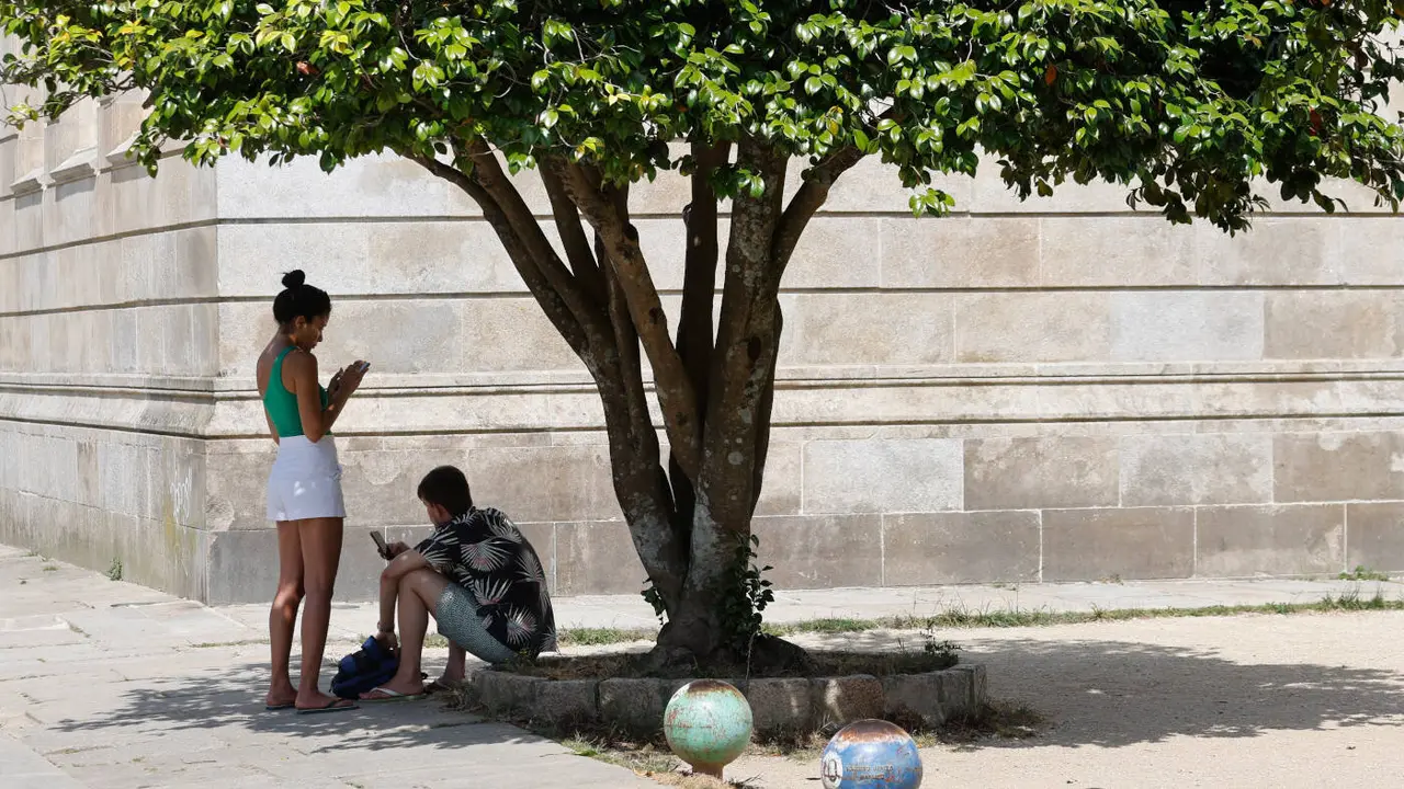 Dos jóvenes se refugian del calor en una sombra de la Alameda de Pontevedra, este martes. GONZALO GARCÍA